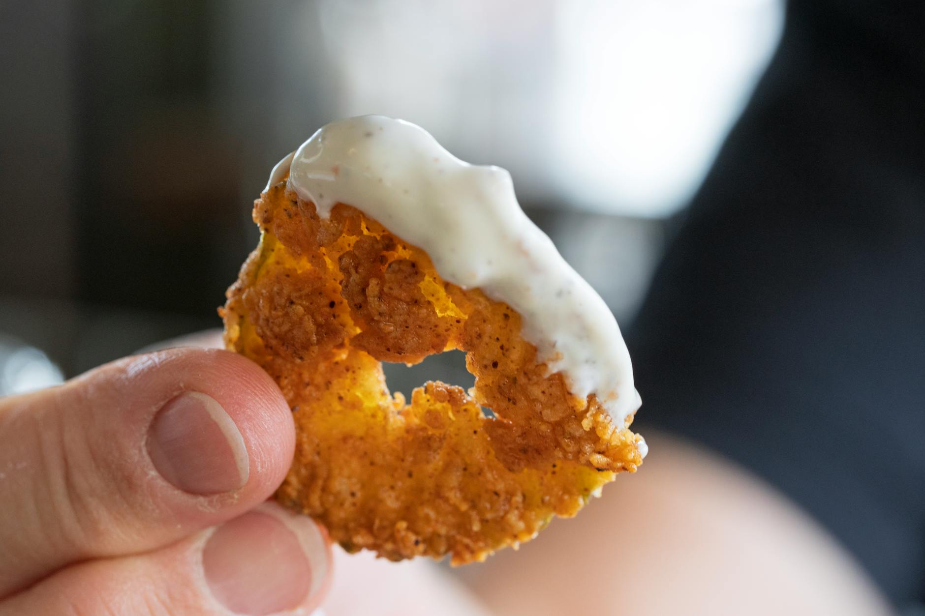 fried onion ring dipped in creamy sauce close up