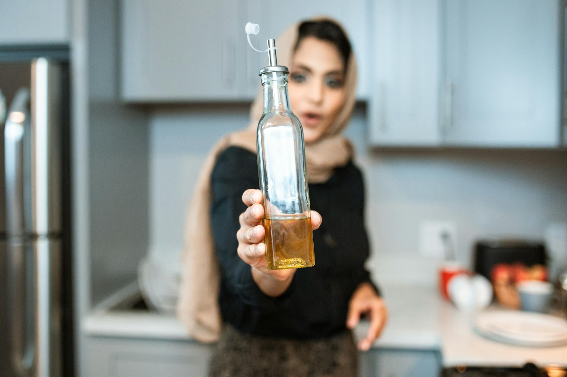 ethnic woman demonstrating bottle of olive oil while cooking