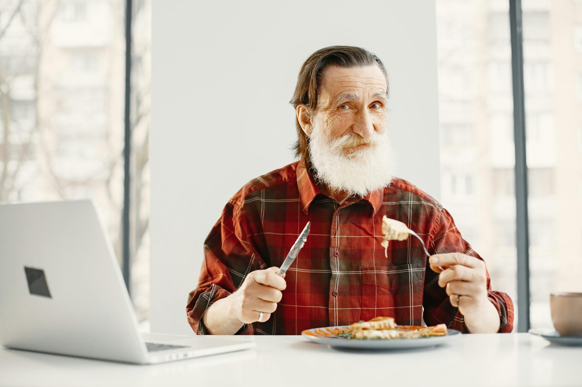 a bearded man eating meal while smiling at the camera