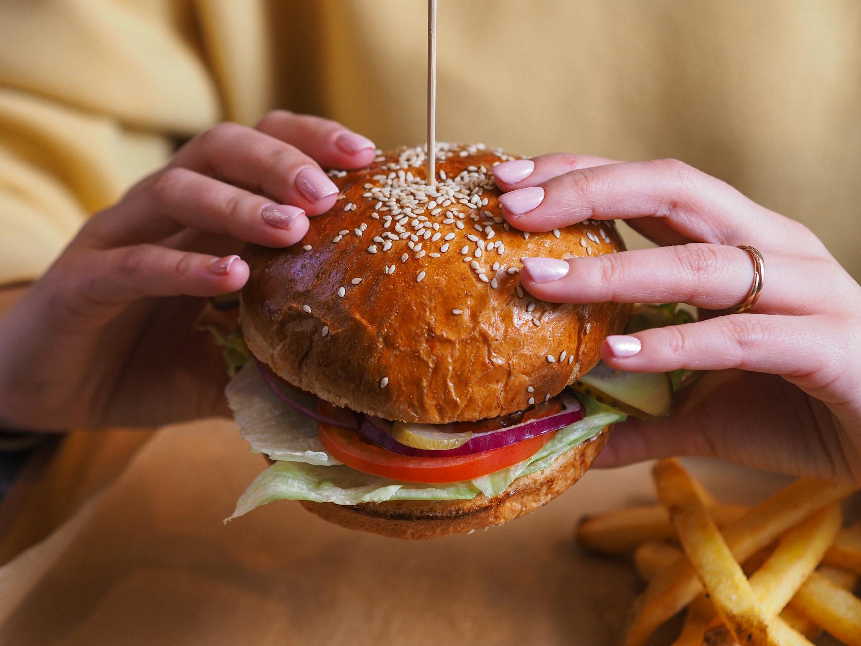 person holding burger with tomato and lettuce