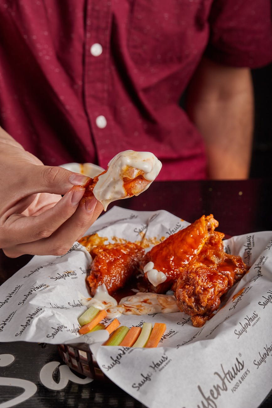 a person holding a chicken wing with sauce