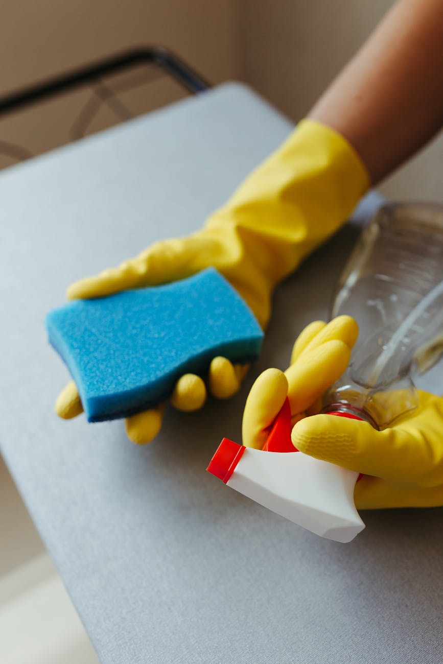 person cleaning surface with blue sponge and spray bottle