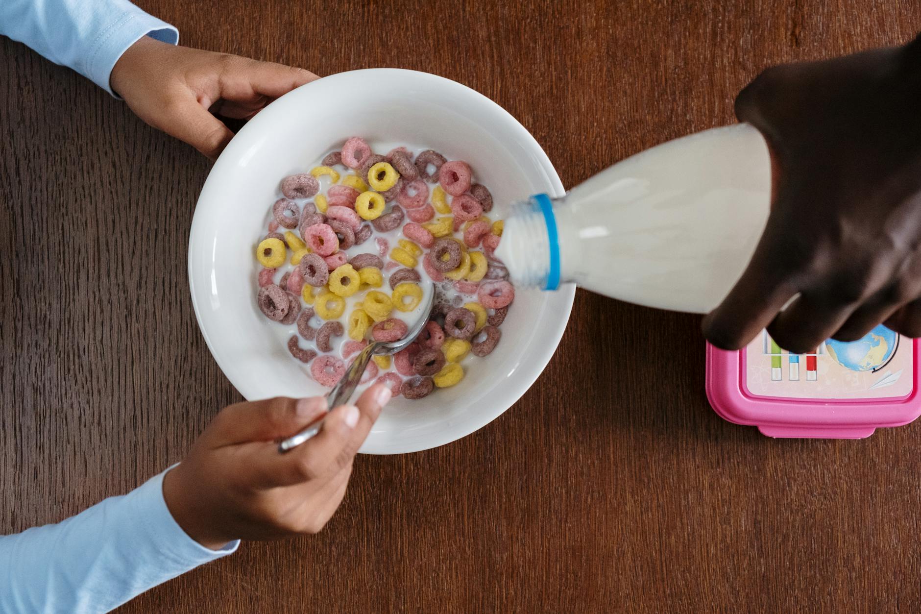 a person pouring milk on bowl of cereals