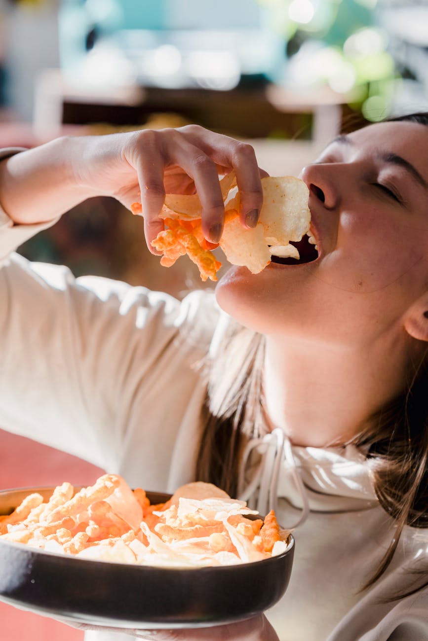 young female eating pile of chips with closed eyes at home
