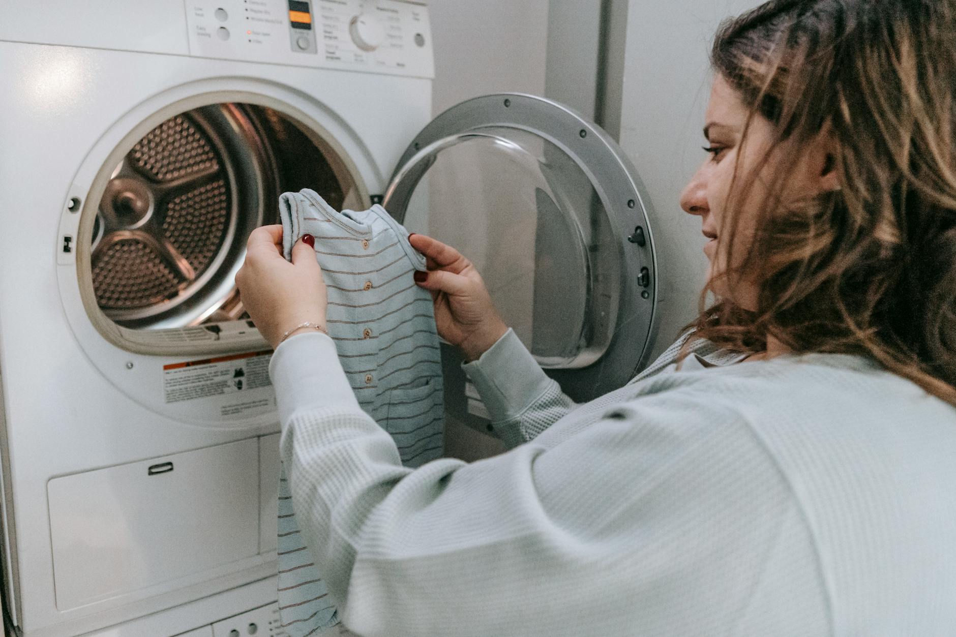 happy mother washing baby clothes in machine