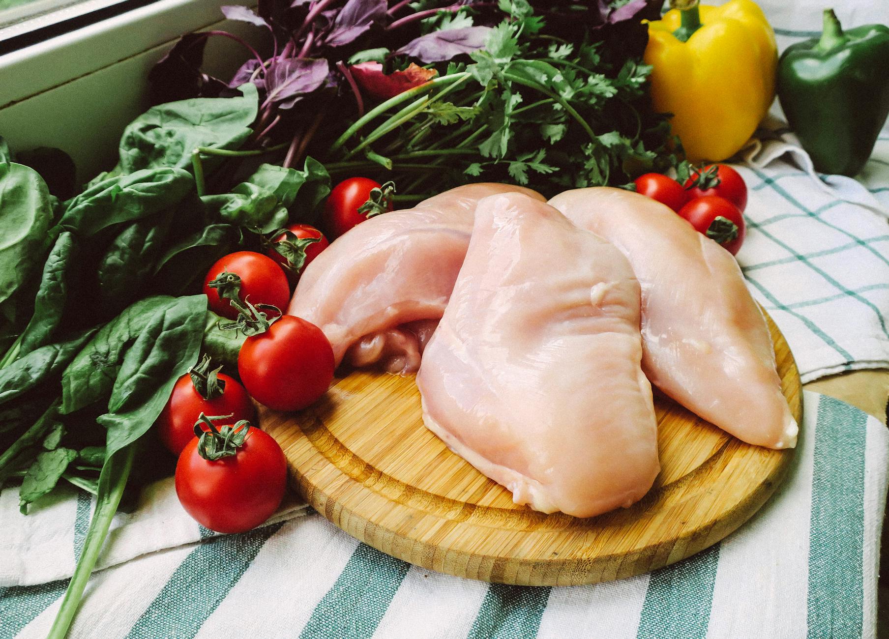 chicken meat on the wooden chopping board beside vegetables