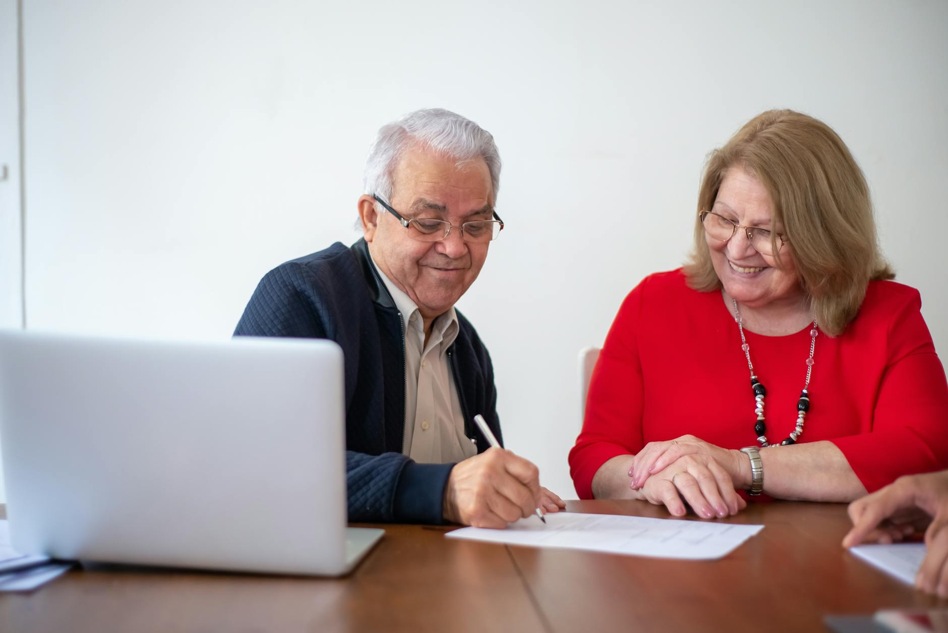 man writing on paper sitting beside woman in red blouse